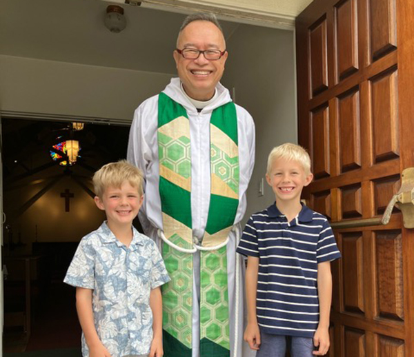 Fr. Joshua poses in front of the church with two children.