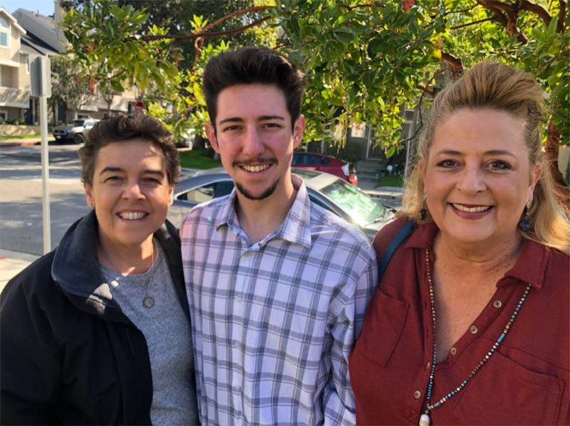 Three smiling parishioners pose on a sunny sidewalk under a tree.