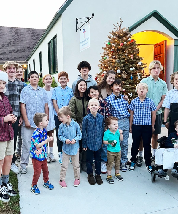 A group of children of various ages pose outside of the church, which is decorated with trees and lights for Christmas.