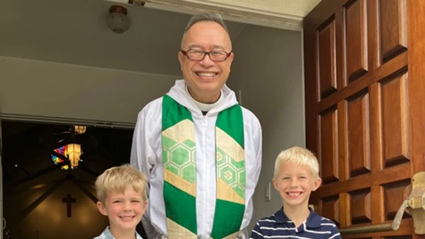 Fr. Joshua poses in front of the church with two children.