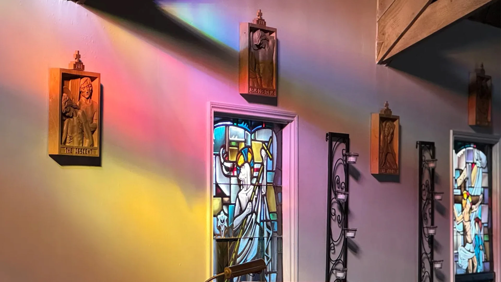 A rainbow of light strikes the stained glass windows and stations of the cross etchings in the sanctuary at dusk.