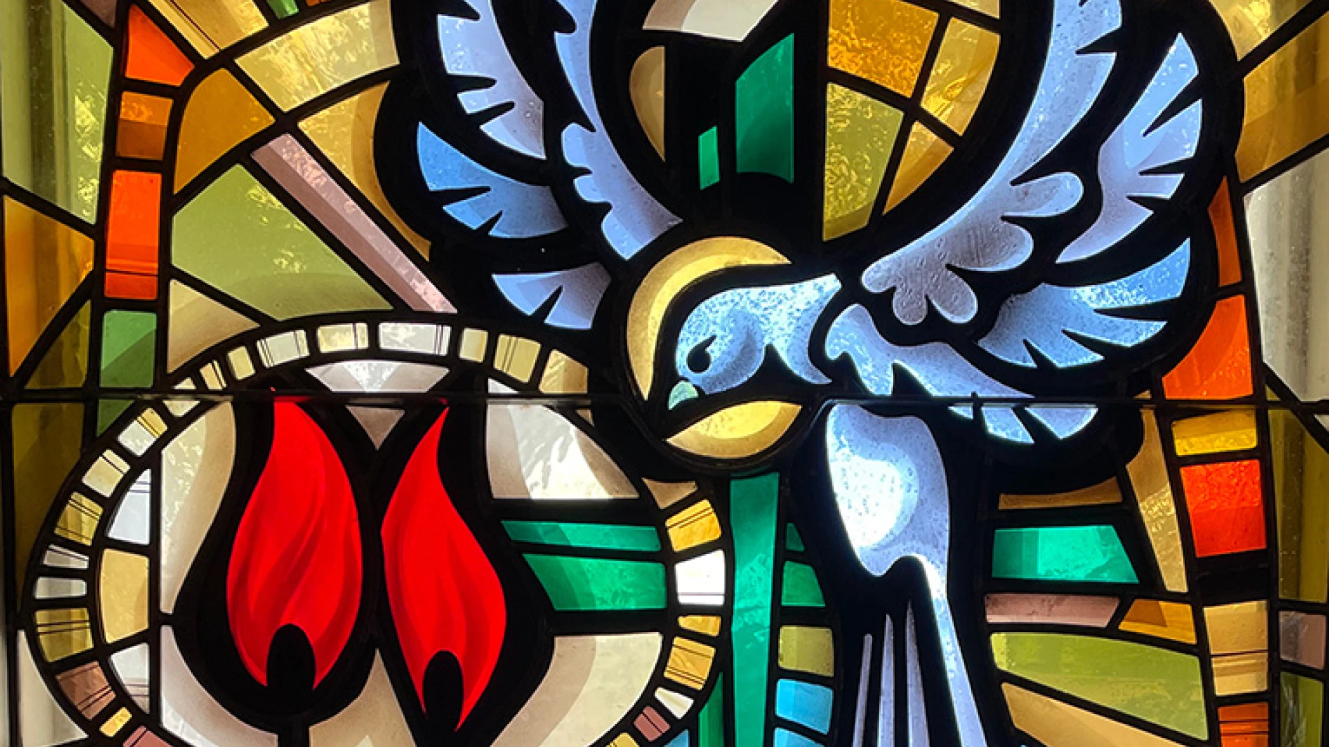 Stained glass window showing a dove, flames, a budding tree and water.