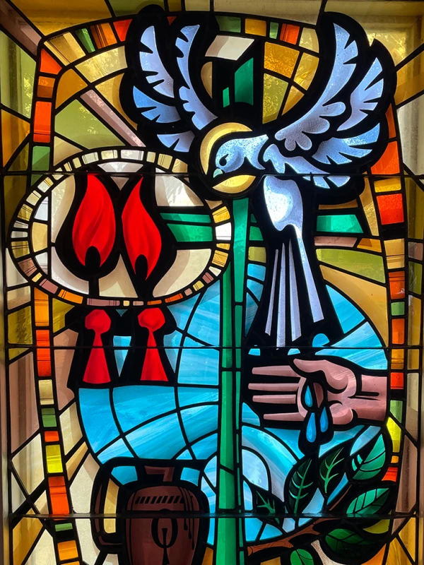 Stained glass window showing a dove, flames, a budding tree and water.