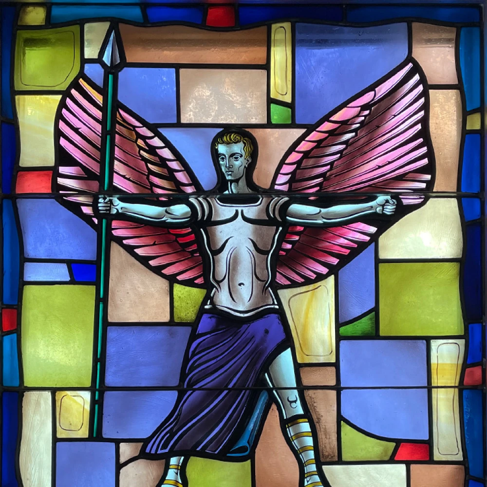 Stained glass window: St. Michael the Archangel stands triumphantly with wings spread over the devil bound at his feet.