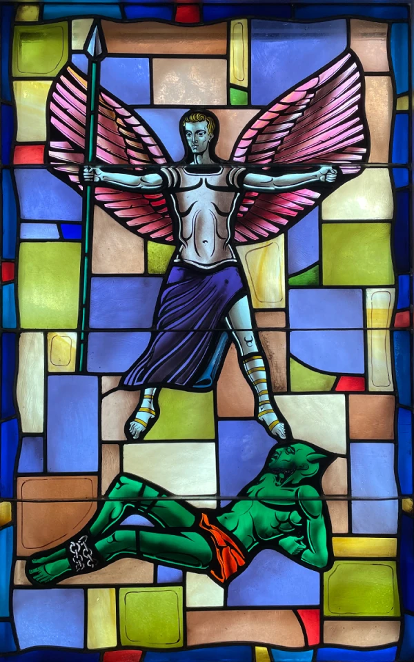 Stained glass window: St. Michael the Archangel stands triumphantly with wings spread over the devil bound at his feet.