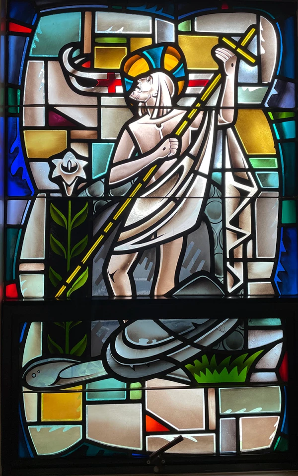 Stained glass window: A risen Jesus holds the cross and rises out of the grave.