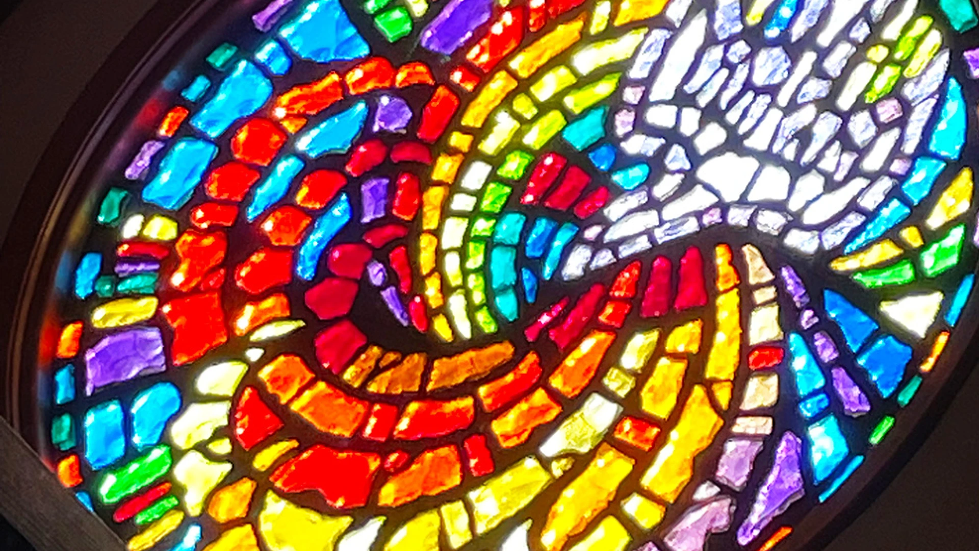 Stained glass window: a circular mosaic of rainbow colored tiles, revealing a dove on one side.