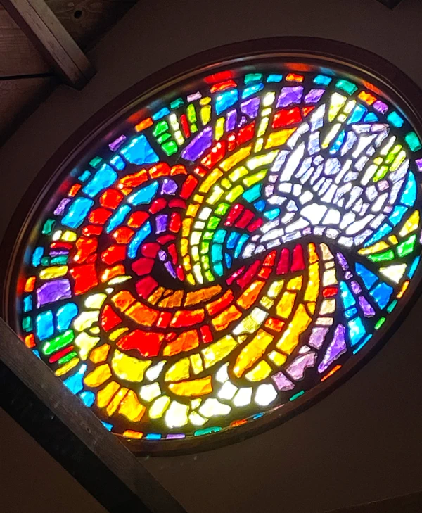 Stained glass window: a circular mosaic of rainbow colored tiles, revealing a dove on one side.
